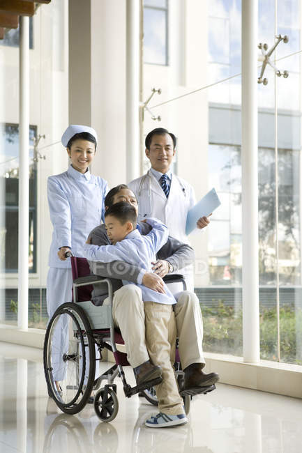 Petit-fils chinois embrassant grand-père en fauteuil roulant avec des médecins — Photo de stock