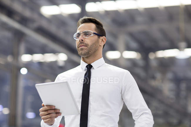 Geschäftsmann mit Schutzbrille hält digitales Tablet in Fabrik — Stockfoto