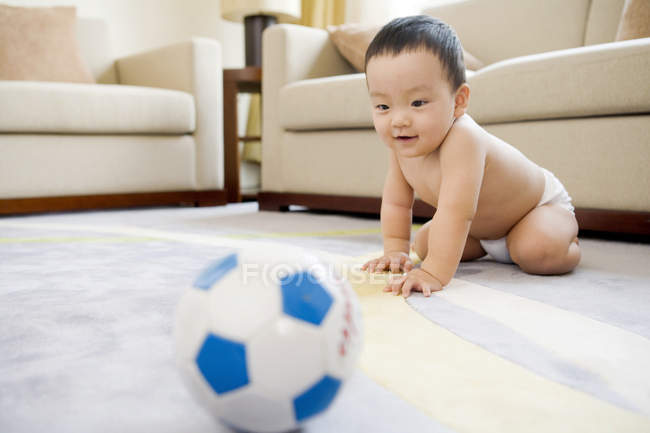 Chinese infant playing with soccer ball in living room — Stock Photo
