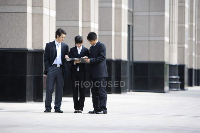 Chinese business people looking down at documents in front of skyscraper — Stock Photo