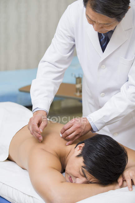Médico chino senior que da acupuntura al paciente masculino - foto de stock