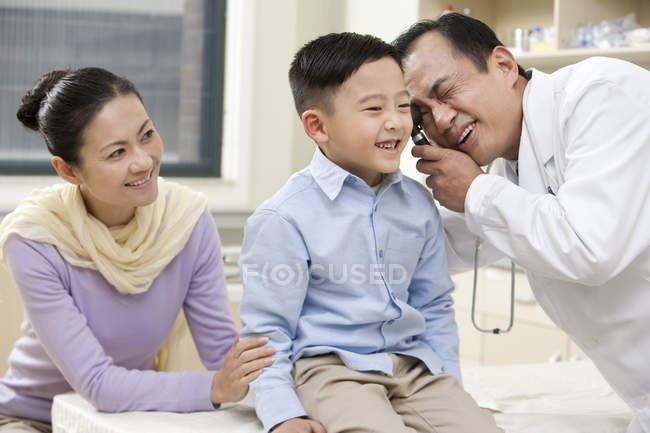Cinese maturo medico esaminando ragazzo con madre in ospedale — Foto stock