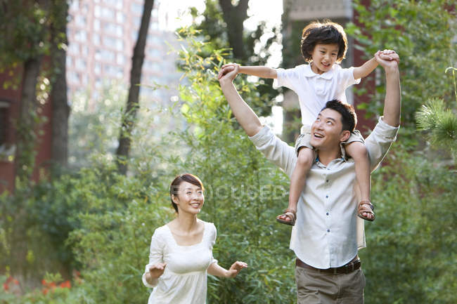 Chino padre llevar hijo en hombros con madre en ciudad jardín - foto de stock