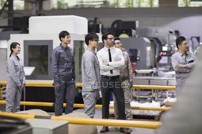 Confident businessman and engineering team looking away at factory — Stock Photo