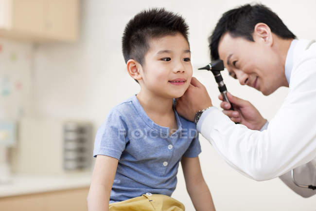 Médico chino examinando oído de niño - foto de stock