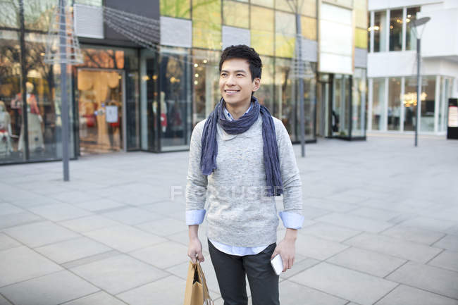 Chinese man in scarf standing with shopping bag on street — Stock Photo