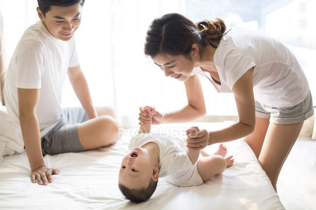 Chinese mother holding hands with baby boy on bed — Stock Photo