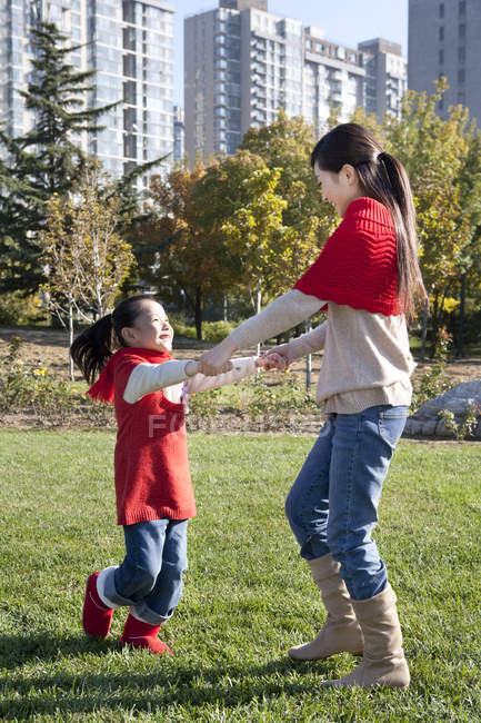 Chinese mother and daughter holding hands and spinning in park — Stock Photo