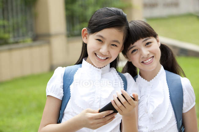 Colegialas chinas sosteniendo teléfono inteligente en el patio de la escuela - foto de stock