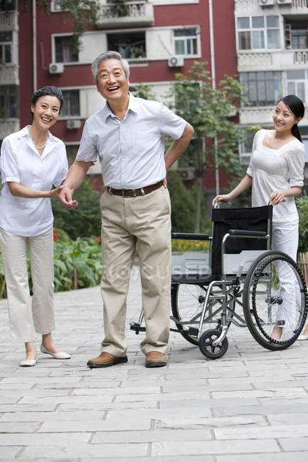 Старший китаец с болью в спине стоит с женщинами на улице — стоковое фото