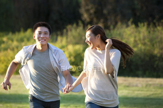 Chinesisches Paar hält Händchen, lacht und rennt im Park — Stockfoto