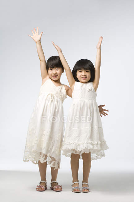 Портрет маленьких китайских девочек с поднятыми на сером фоне руками — стоковое фото