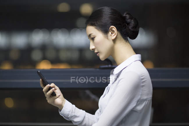 Vue latérale de la femme d'affaires chinoise utilisant un smartphone dans un immeuble de bureaux — Photo de stock