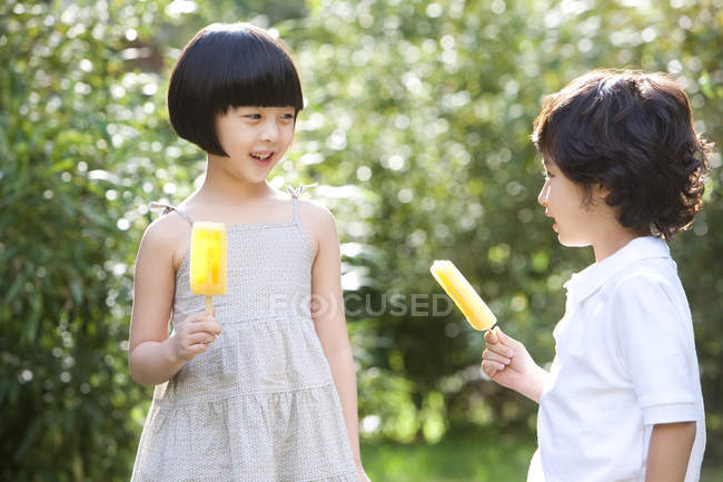 Chinese children holding ice pops in summer garden — Stock Photo