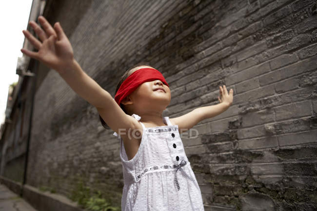Chica china con los ojos vendados jugando a las escondidas en el callejón - foto de stock
