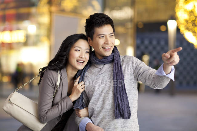 Китаец указывает на витрину магазина во время прогулки с женщиной — стоковое фото