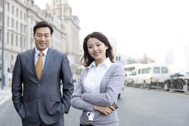 Chinese business people standing with arms crossed on street in financial district — Stock Photo