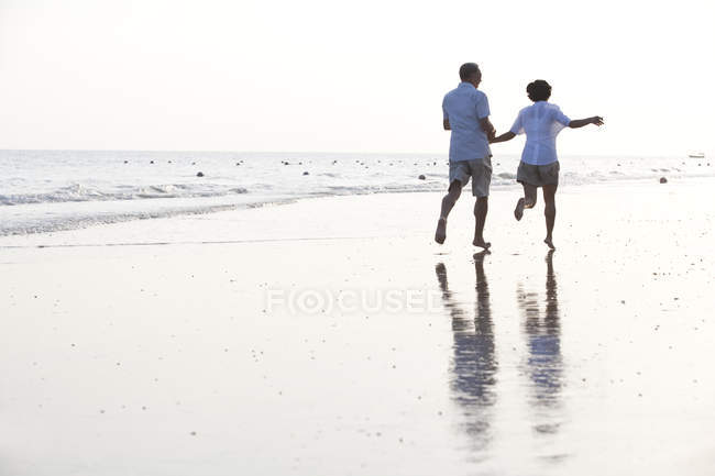 Старшая китайская пара бегает по пляжному песку — стоковое фото