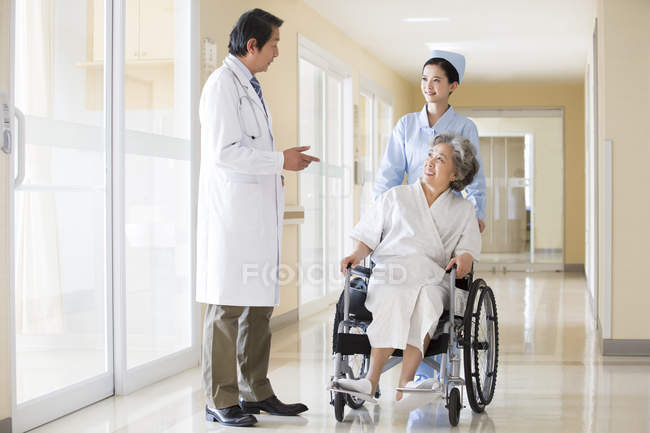 Trabajadores médicos chinos cuidando a una mujer mayor en silla de ruedas - foto de stock