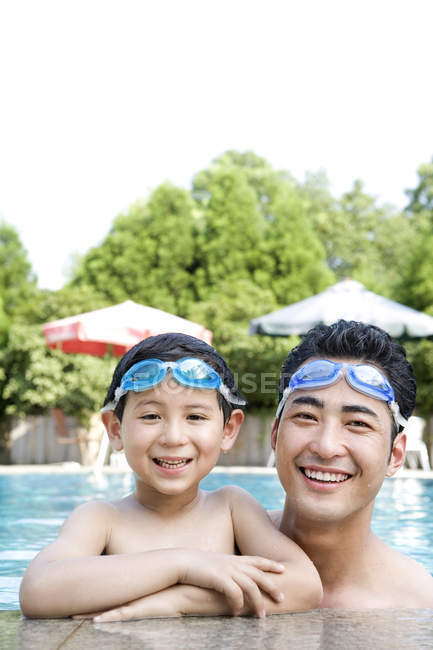 Padre e hijo chinos en gafas de natación en la piscina - foto de stock