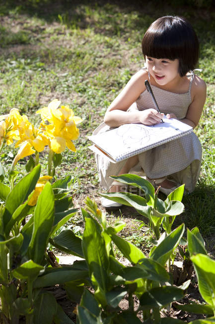 Pequena menina chinesa desenho flores amarelas no jardim — Fotografia de Stock