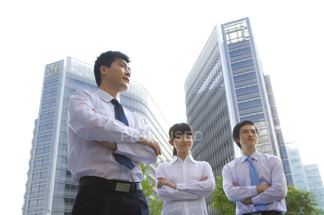 Chinese business people with arms crossed in front of skyscrapers — Stock Photo
