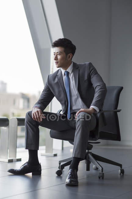Hombre de negocios chino mirando por la ventana en la oficina - foto de stock