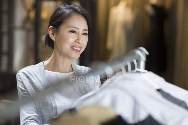 Reife chinesische Boutique-Besitzerin steht am Kleiderständer — Stockfoto