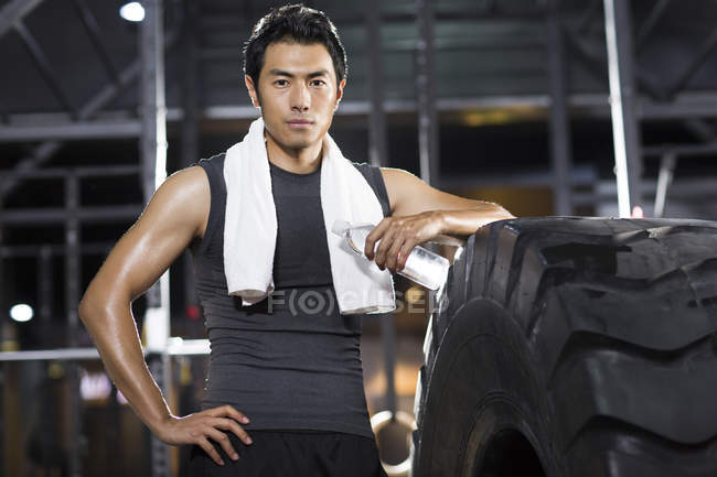 Chinese man resting at gym with towel and water — Stock Photo