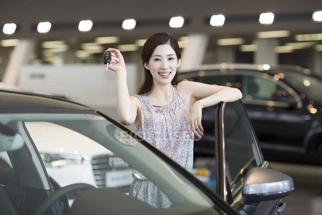 Chinese woman holding keys to new car in showroom — Stock Photo