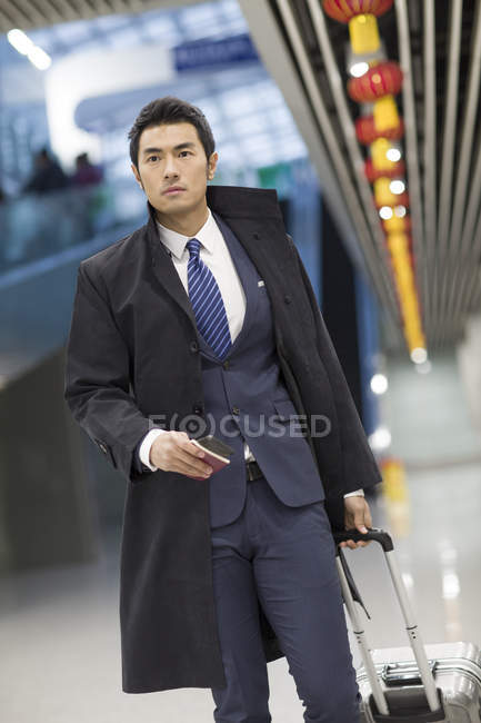 Hombre de negocios chino caminando en el aeropuerto con maleta y pasaporte - foto de stock