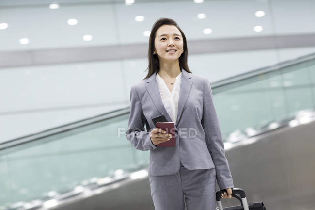 Empresaria china caminando en aeropuerto con maleta y pasaporte - foto de stock
