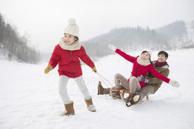 Chinese girl pulling sled with parents on snow — Stock Photo