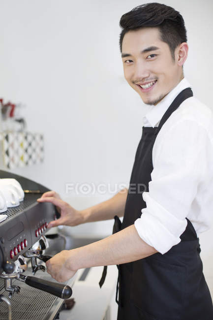 Chinese barista standing at coffee maker and looking in camera — Stock Photo