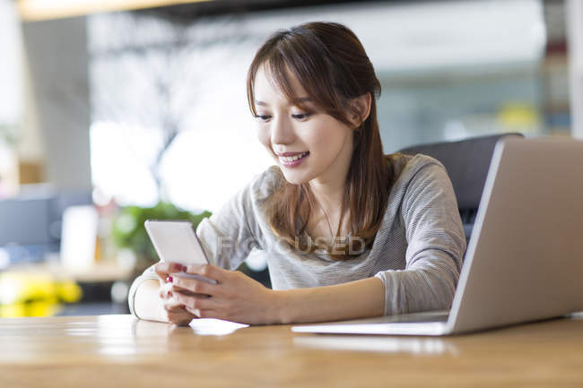 Chinese woman using smartphone at office desk — Stock Photo
