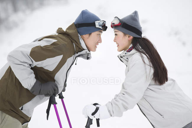 Chinese couple standing face to face with ski poles — Stock Photo