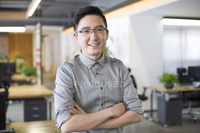 Chinese man standing in office with arms folded — Stock Photo