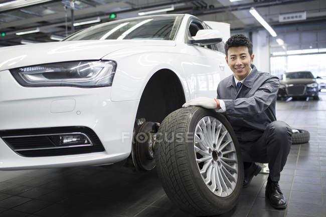 Chinese auto mechanic holding car wheel in workshop — Stock Photo