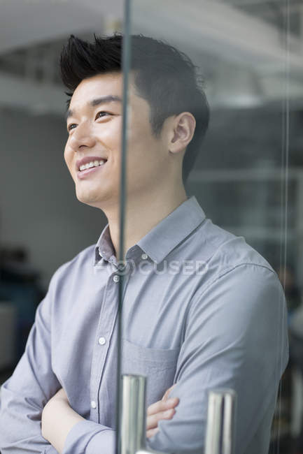 Hombre de negocios chino de pie en la oficina con los brazos cruzados - foto de stock