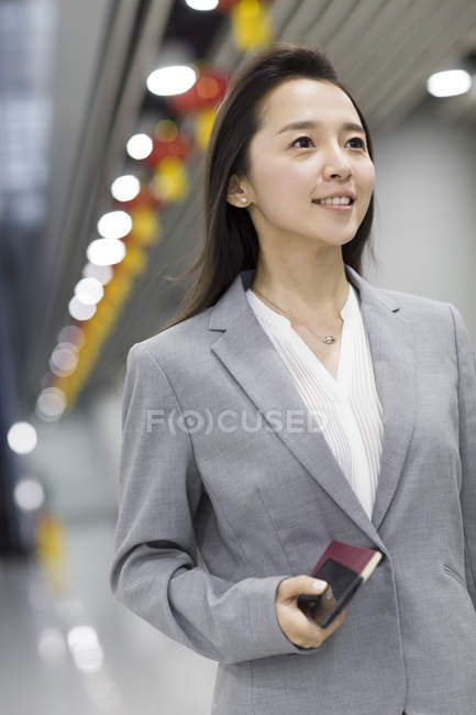 Chinese businesswoman holding passport and smartphone in airport — Stock Photo