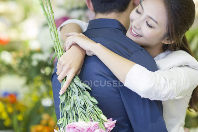 Chinese woman embracing boyfriend with flowers, close-up — Stock Photo