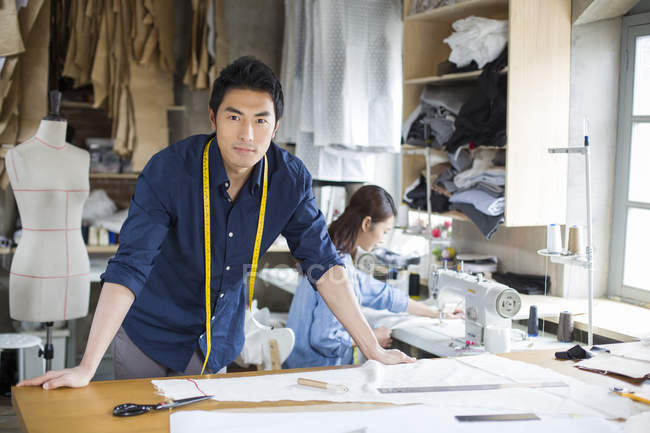 Chinês designer de moda masculina inclinando-se na mesa em estúdio — Fotografia de Stock