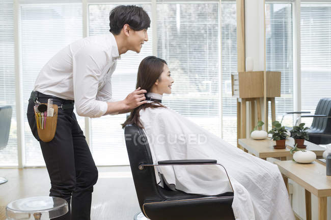 Barbero chino hablando con el cliente en peluquería - foto de stock