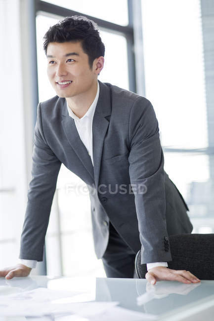 Китайский бизнесмен опирается на стол в офисе — стоковое фото