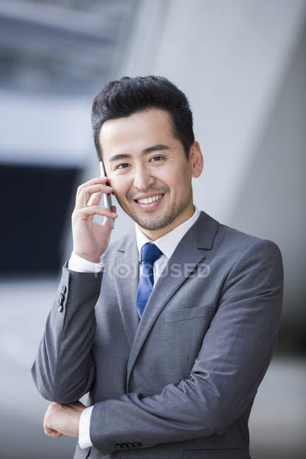 Uomo d'affari cinese che parla al telefono e guarda in macchina fotografica — Foto stock