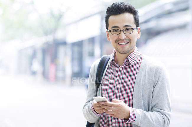 Hombre chino sosteniendo teléfono inteligente y sonriendo - foto de stock