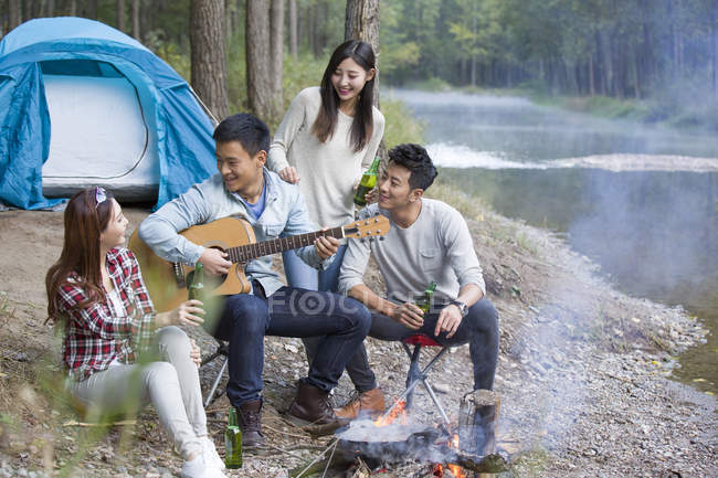 Amigos chineses sentados ao redor da fogueira e tocando guitarra — Fotografia de Stock
