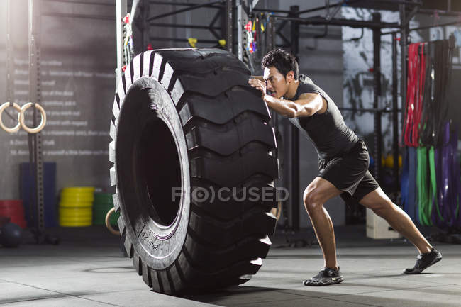 Uomo cinese spingendo grande pneumatico in palestra crossfit — Foto stock