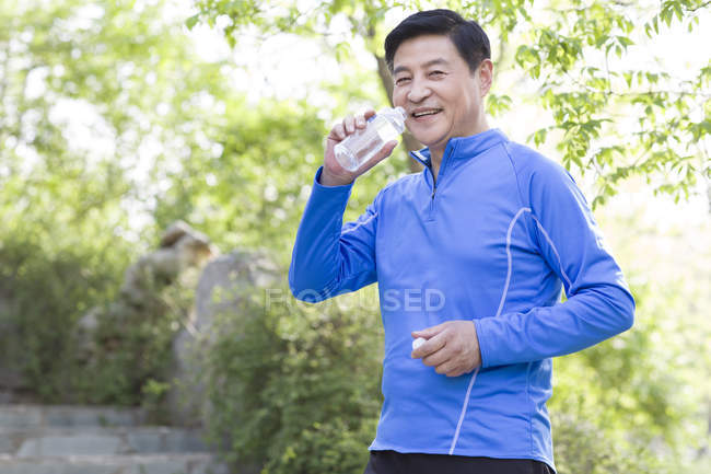 Mature chinese man drinking water after exercising — Stock Photo