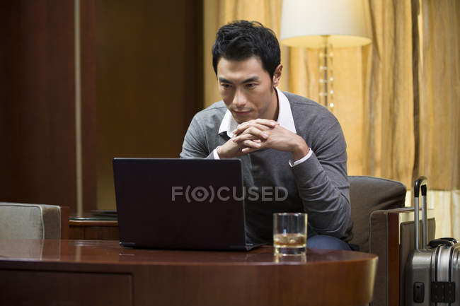 Uomo d'affari cinese che utilizza il computer portatile a tavola in camera d'albergo — Foto stock